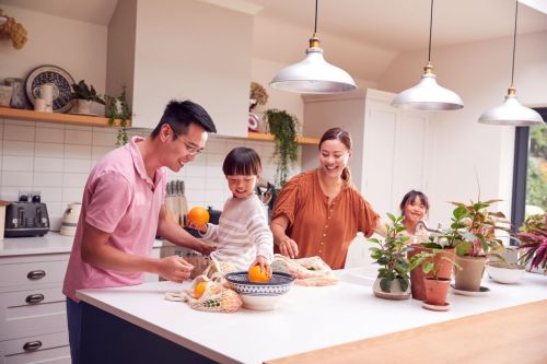 Smiling family with man, boy sitting on counter, woman, girl in kitchen holding local groceries