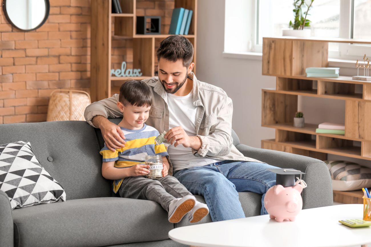 Man and boy sit on couch putting money into jar to save for education