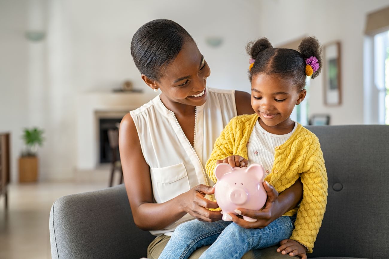 smiling woman and girl with piggy bank saving money