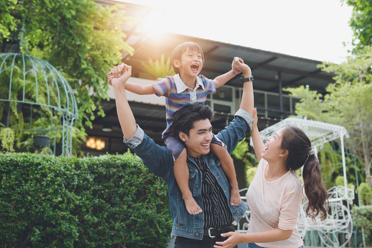 Smiling Asian family with boy sitting on man's shoulders and woman holding boy's hand.