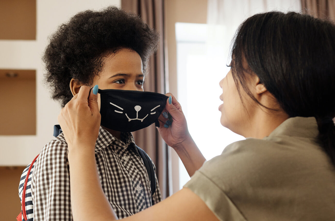 Mother putting face mask on her son to stay safe from COVID-19