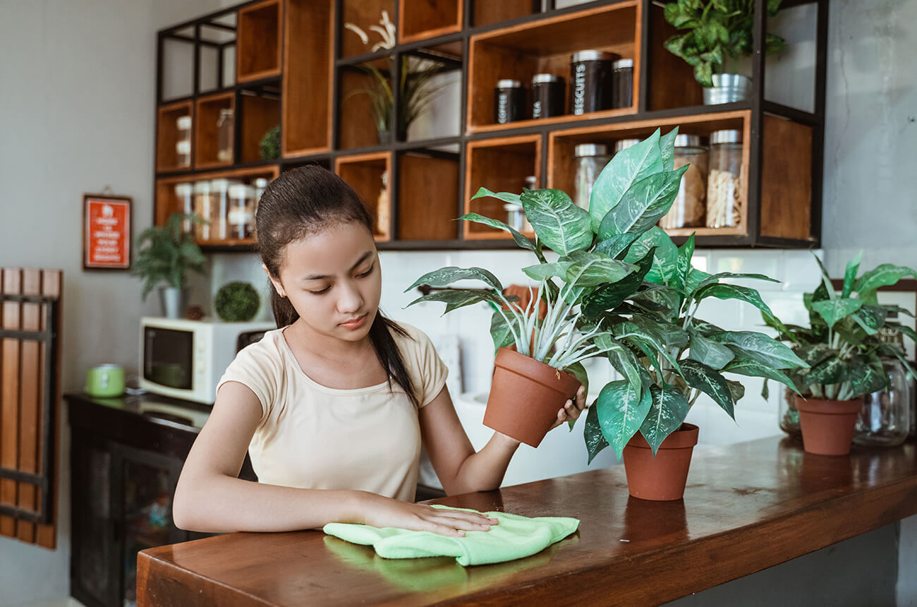 A teenage girl taking care of plants and wiping a table clean for her chores