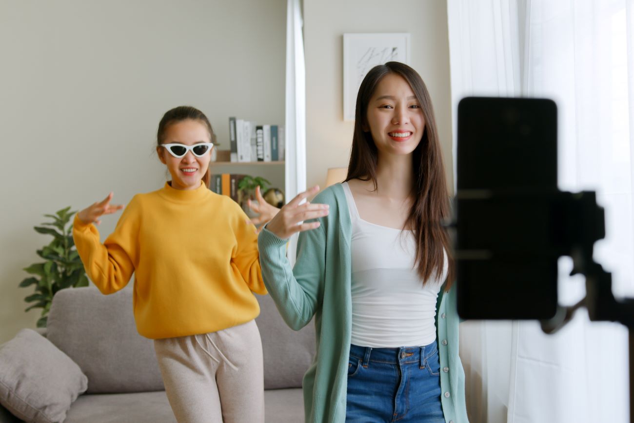 Two teen girls performing TikTok dance and filming themselves with smartphone
