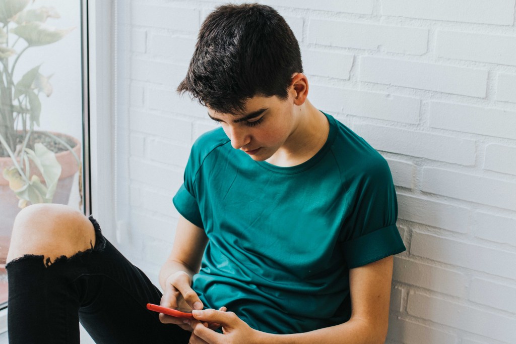 A teen boy using Facebook on his phone