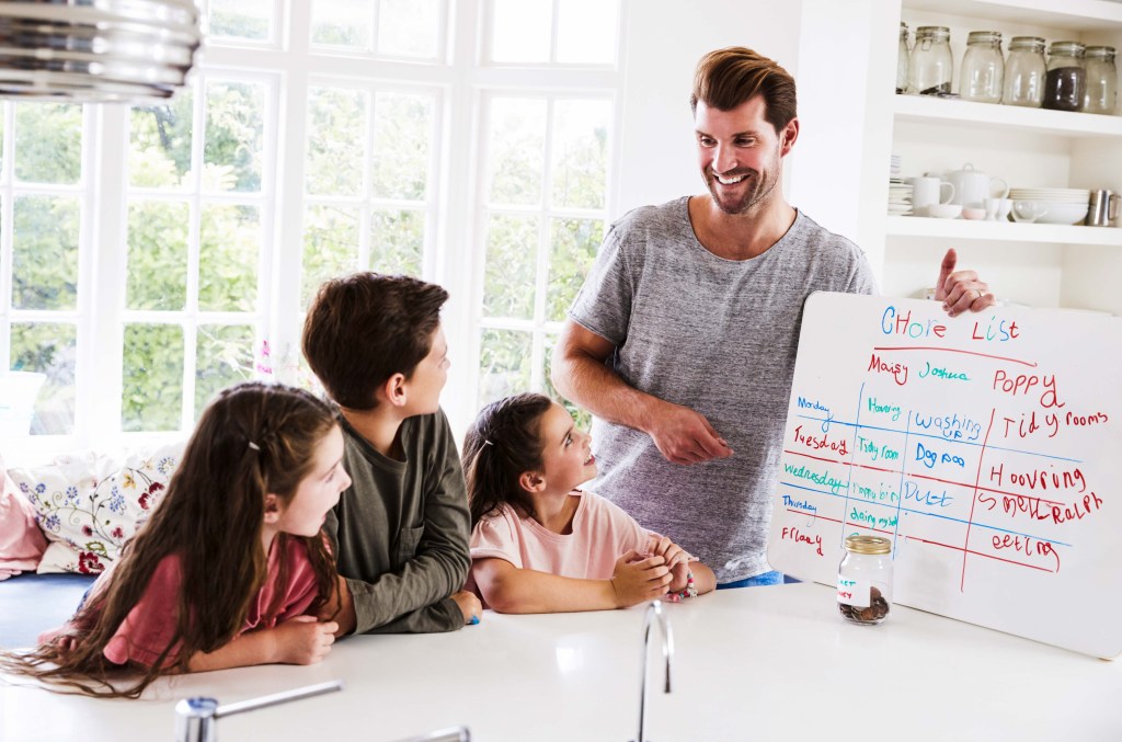 A father showing his kids the chore list board