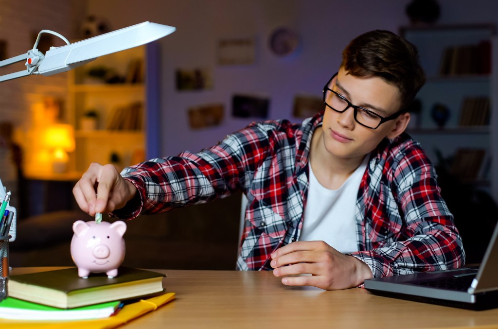 A teen boy saving money in a piggy bank