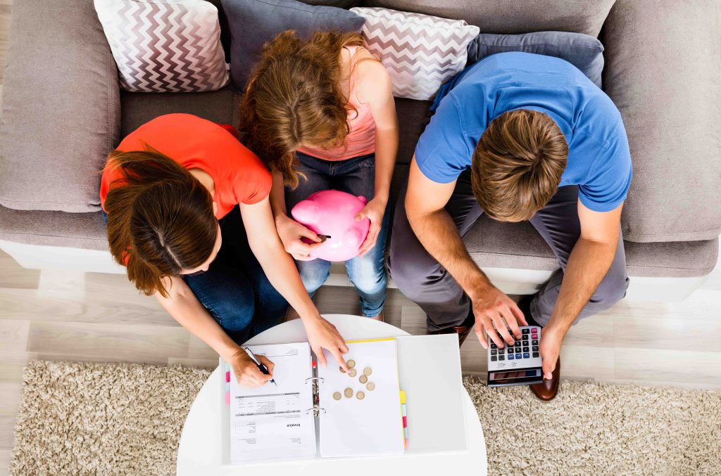 A mom and dad explaining banking to their kids with coins and a calculator.