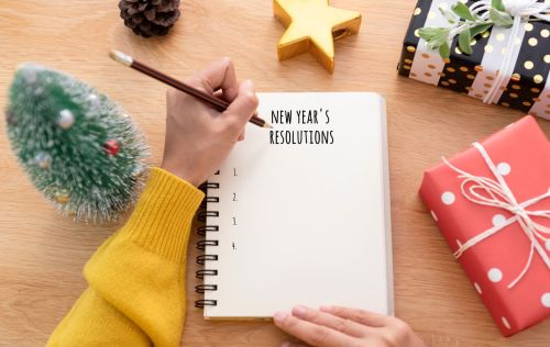 Person wearing yellow sweater writing new year's resolutions surrounded by holiday gifts and decorations