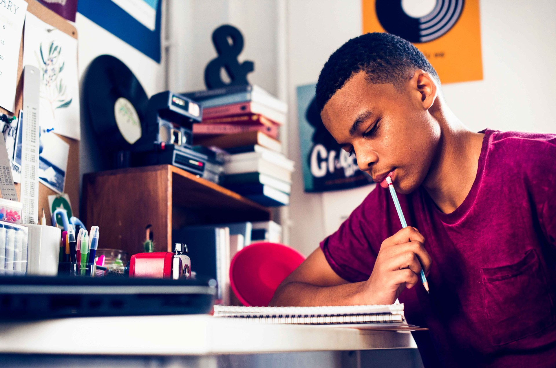 Teenage boy in a bedroom doing work thinking