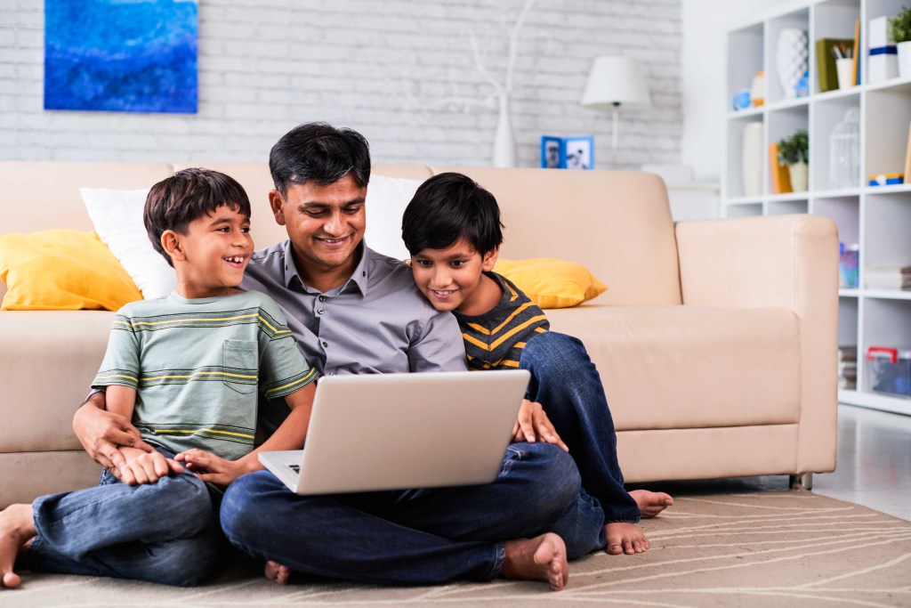 A dad and his two kids staying warm inside watching a movie on a laptop