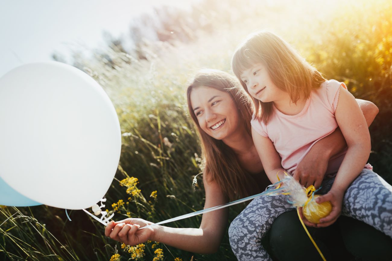 Woman holds balloon and hugs girl with Down Syndrome