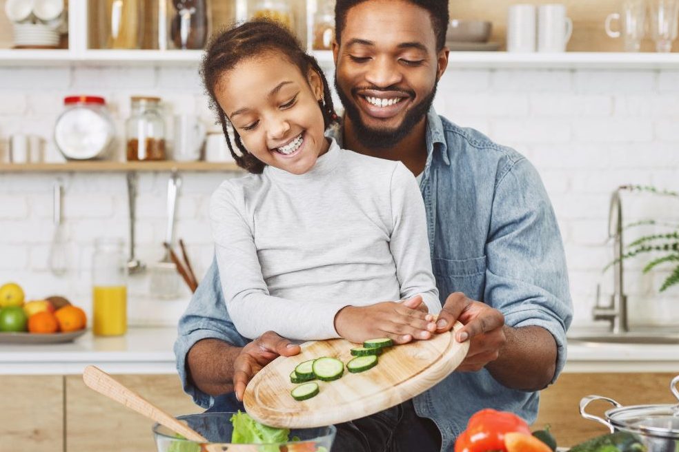 Smiling Black girl and father preparing vegetables in kitchen