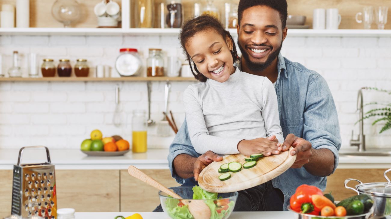 Smiling Black girl and father preparing vegetables in kitchen