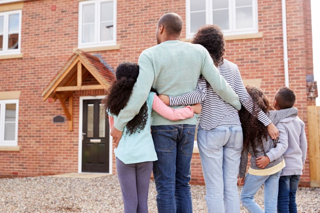 Black family embracing each other and facing brick house