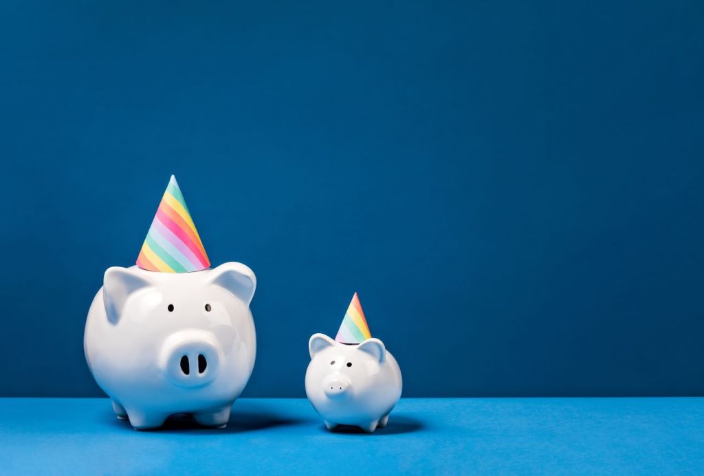 Two white piggy banks with rainbow coloured party hats