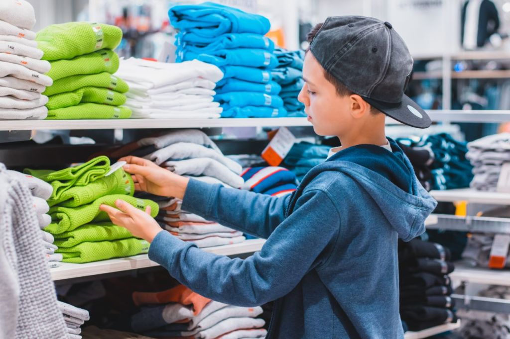 Boy with baseball looking through pile of green sweaters