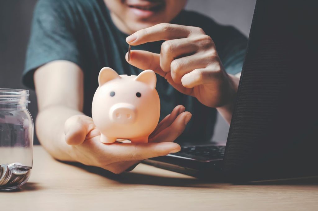 A teen boy putting a coin in a piggy bank