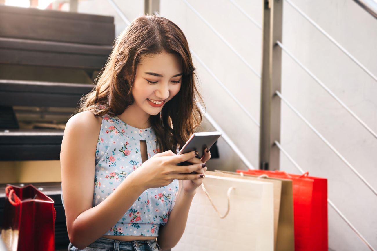 Smiling girl holds phone, surrounded by shopping bags