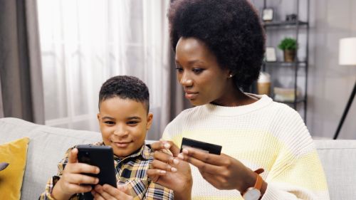 woman holding credit card sits next to boy holding phone