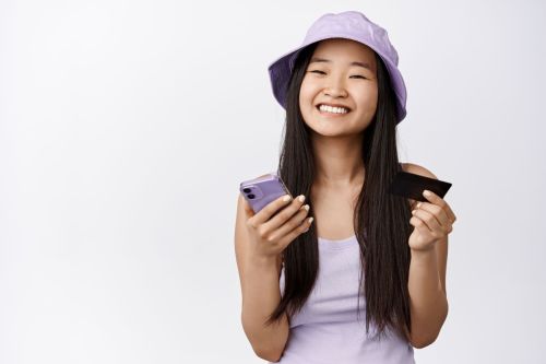 Smiling girl in purple hat holds phone and bank card