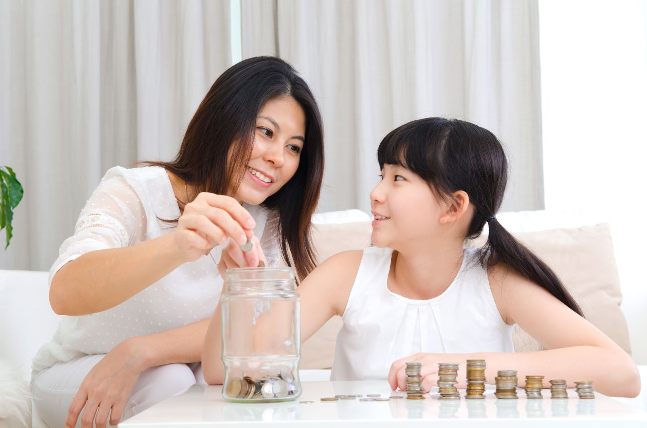 Smiling Asian woman and girl sitting in front of pile of coins counting them out