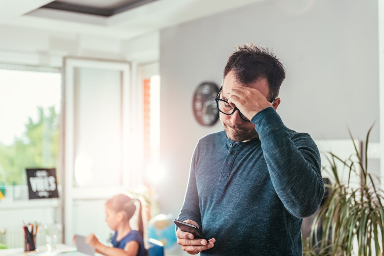 Man looks at phone worried about debt with girl in background