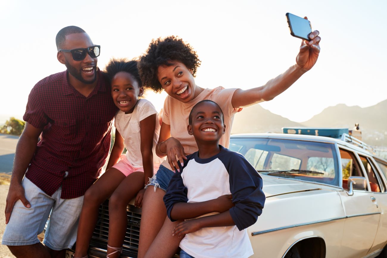 Smiling black family sitting against car and looking at iPhone