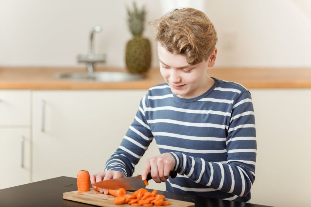 Boy in stripped shirt cutting carrots on cutting board