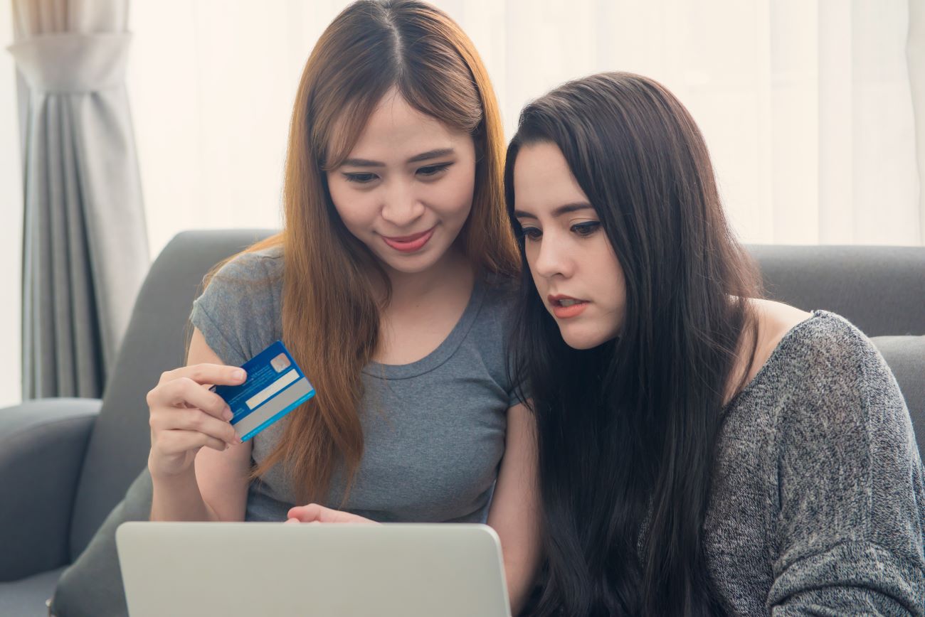Two teen girls sitting on couch with cash card looking at laptop