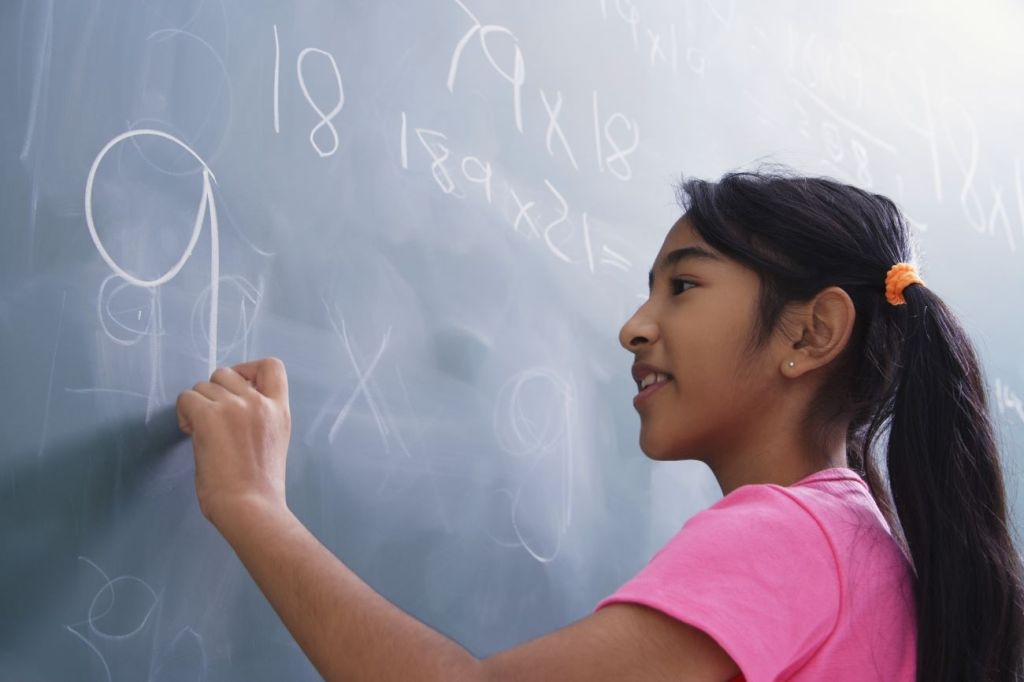 A young girl writing on a chalkboard and learning about financial literacy in a classroom