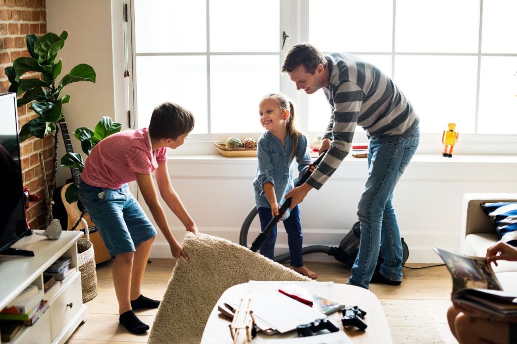 Two young kids vacuuming and doing chores with their dad
