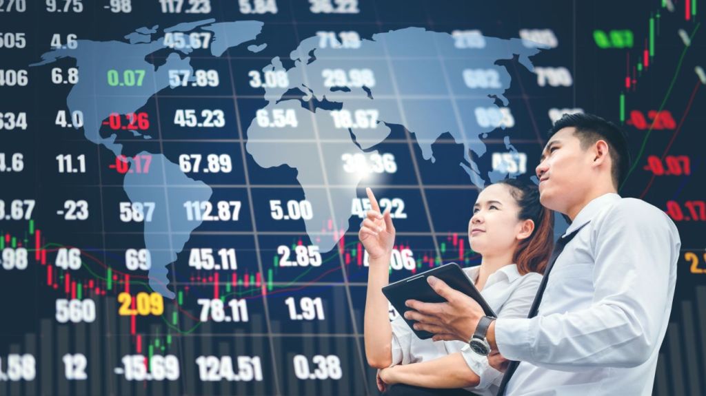 A man and a teen girl stand in front of stock board at stock exchange