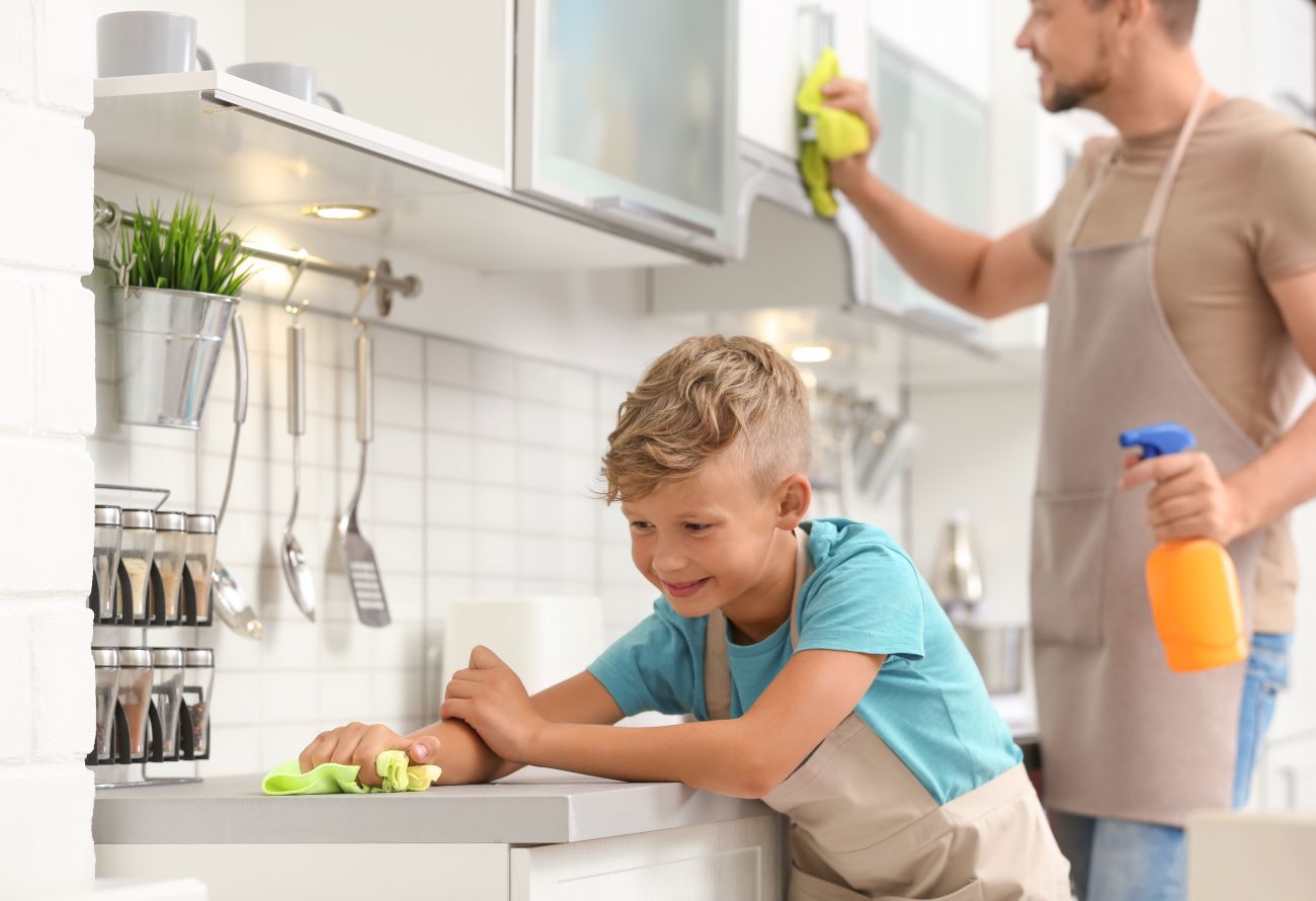 Boy and man wearing aprons spring clean a kitchen