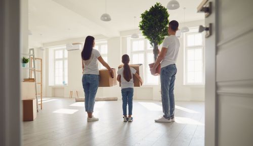 Family hold boxes and stand in their new home