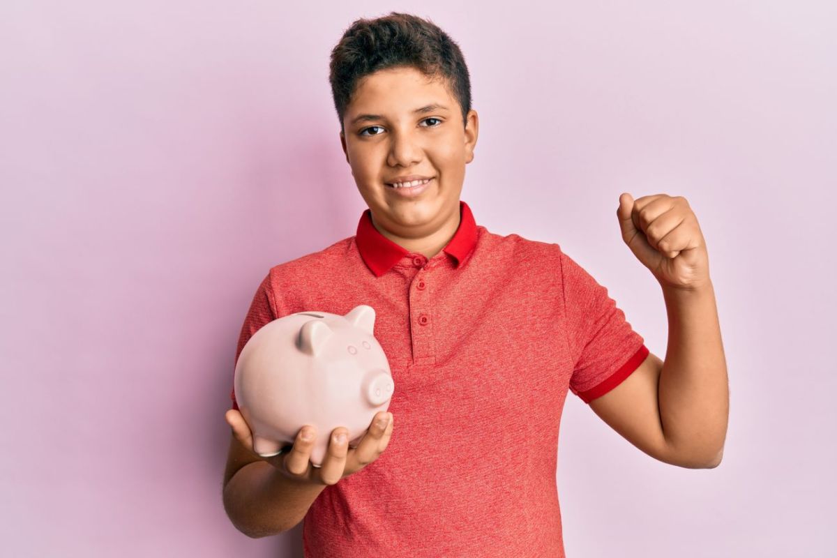 Boy holds piggy bank and pumps fist as he saves to invest his money