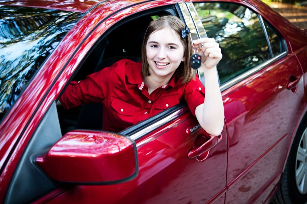 Smiling teen girl sits in red car holding key to her new vehicle