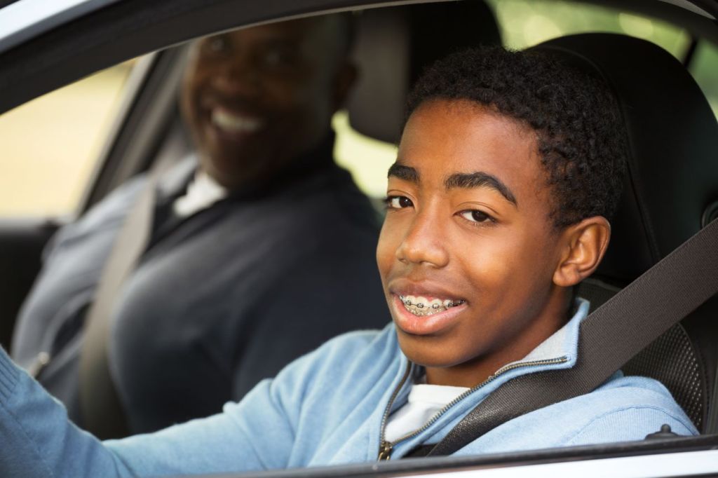 Smiling teen boy sits in driver's seat of car next to smiling man