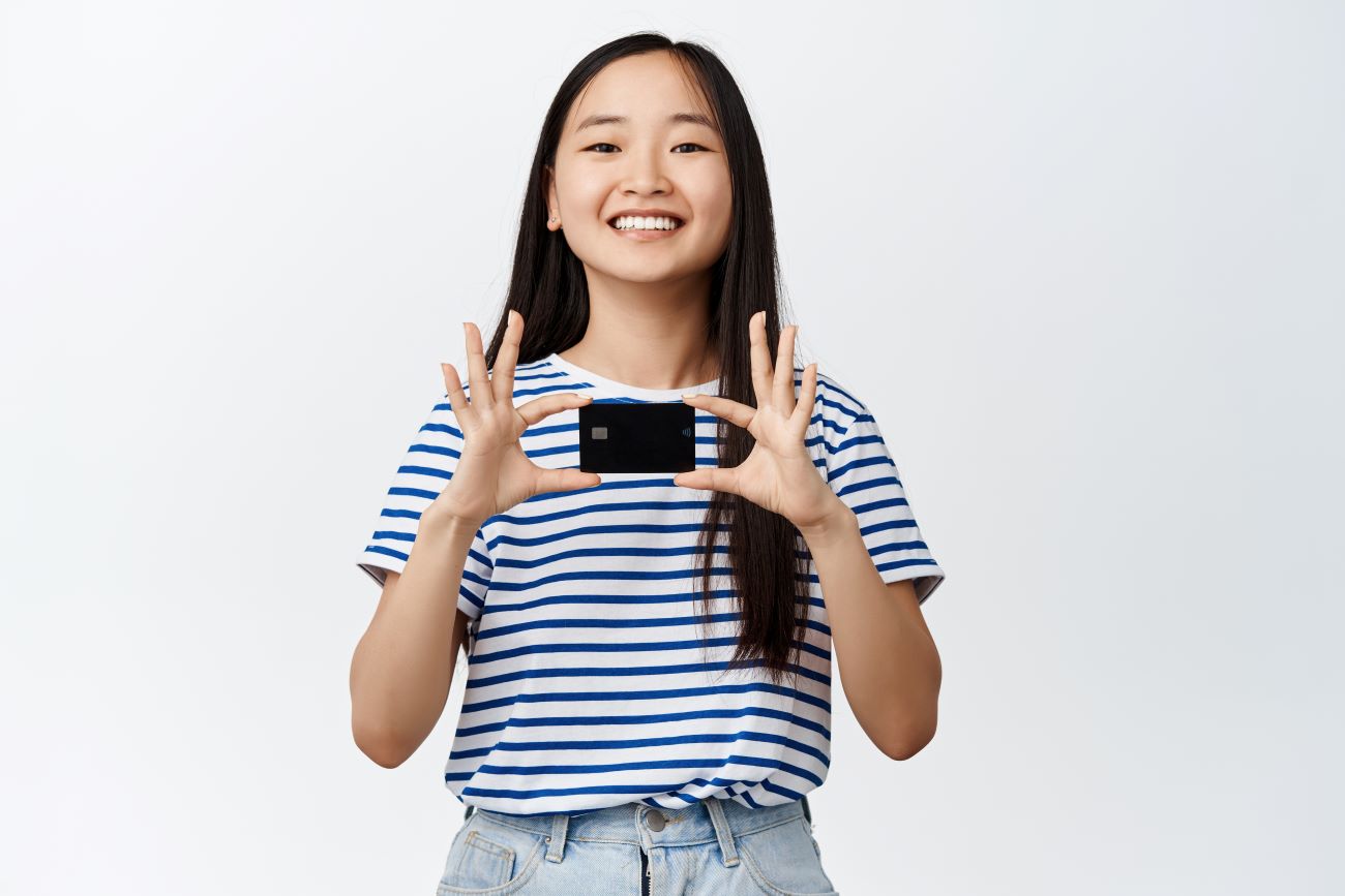 Smiling Asian girl holds up credit card, which is a type of debt