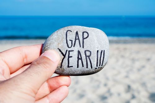 Person holding a rock that says "Gap Year" by ocean