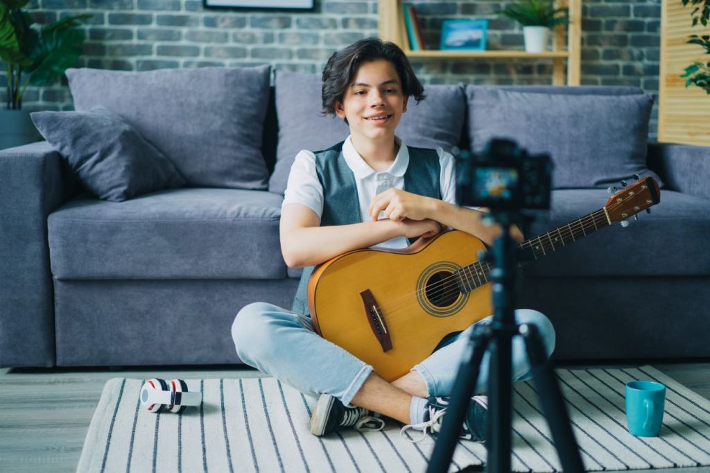 A young teen boy recording a YouTube video for how to play a guitar