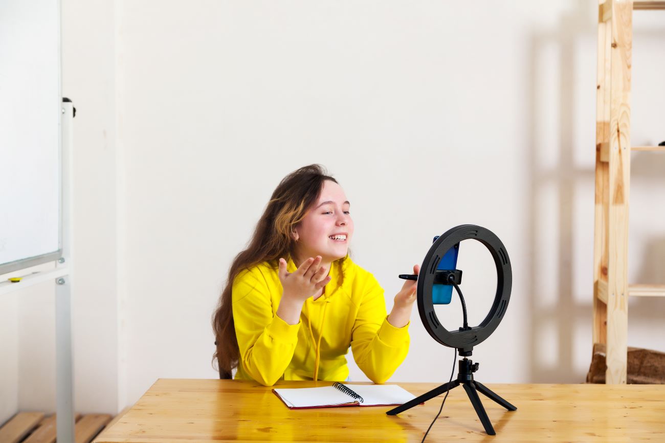 Teen girl in yellow shirt sits behind ring light recording a video for her YouTube channel