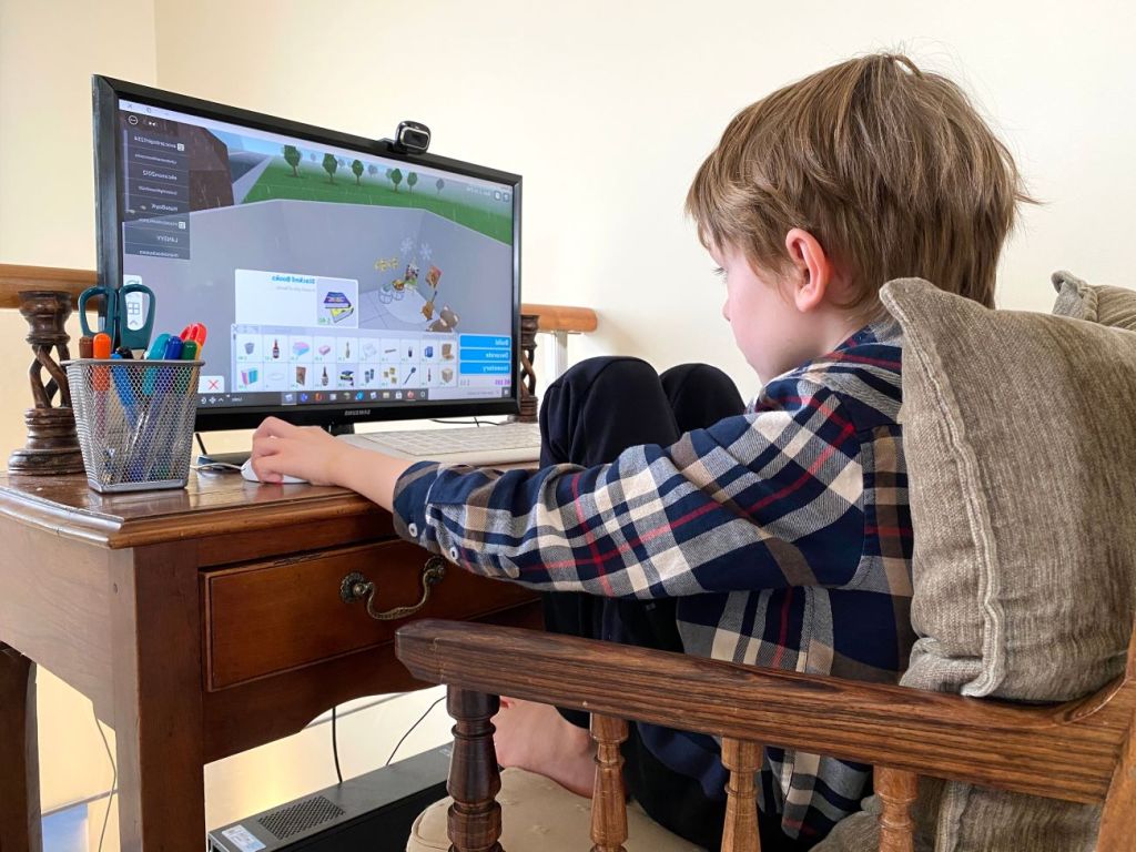 Boy sits at desk playing Roblox on computer screen