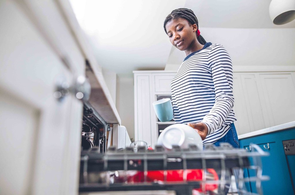 Teenager loading dishwasher as part of her weekly chores