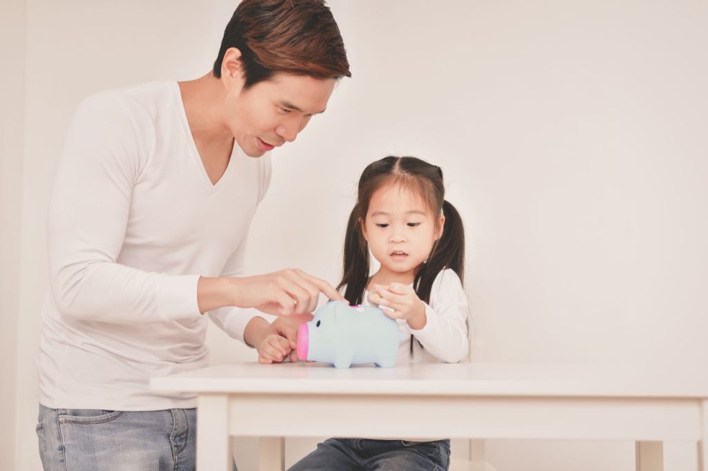 A father teaching his daughter how to save money using coins from a coin jar
