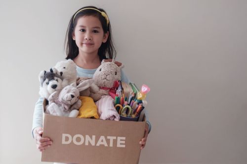 Girl holds cardboard box that says donate filled with toys and stationery supplies