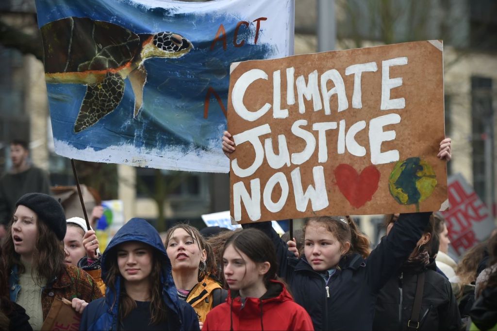 A group of teens marching with a sign that says "Climate Justice Now"