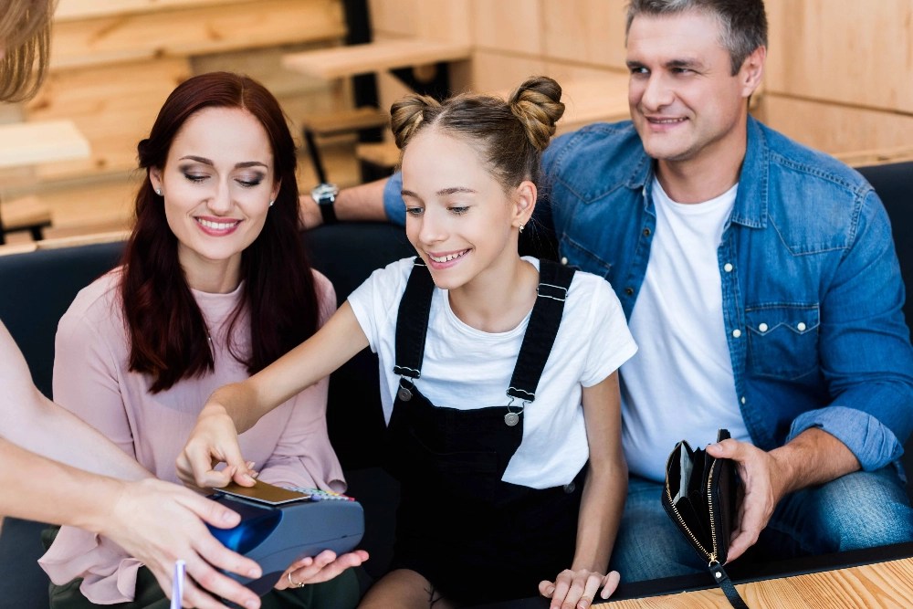 A preteen girl paying for a bill with her parents