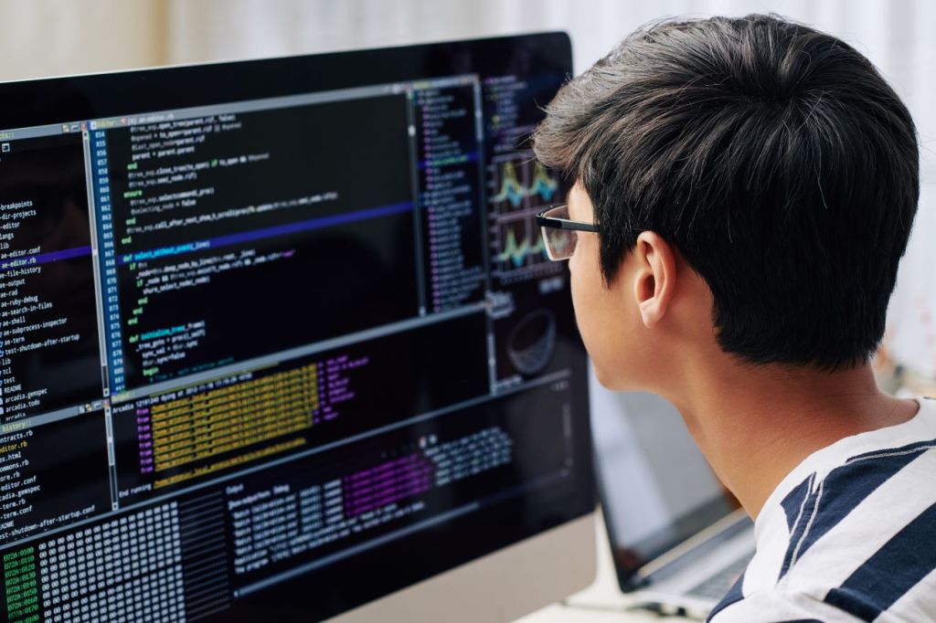 Teenage boy sitting at computer screen coding