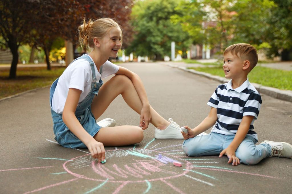 Teen girl looking after boy drawing with chalk