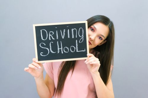 Teen girl holding up chalkboard sign that says driving school